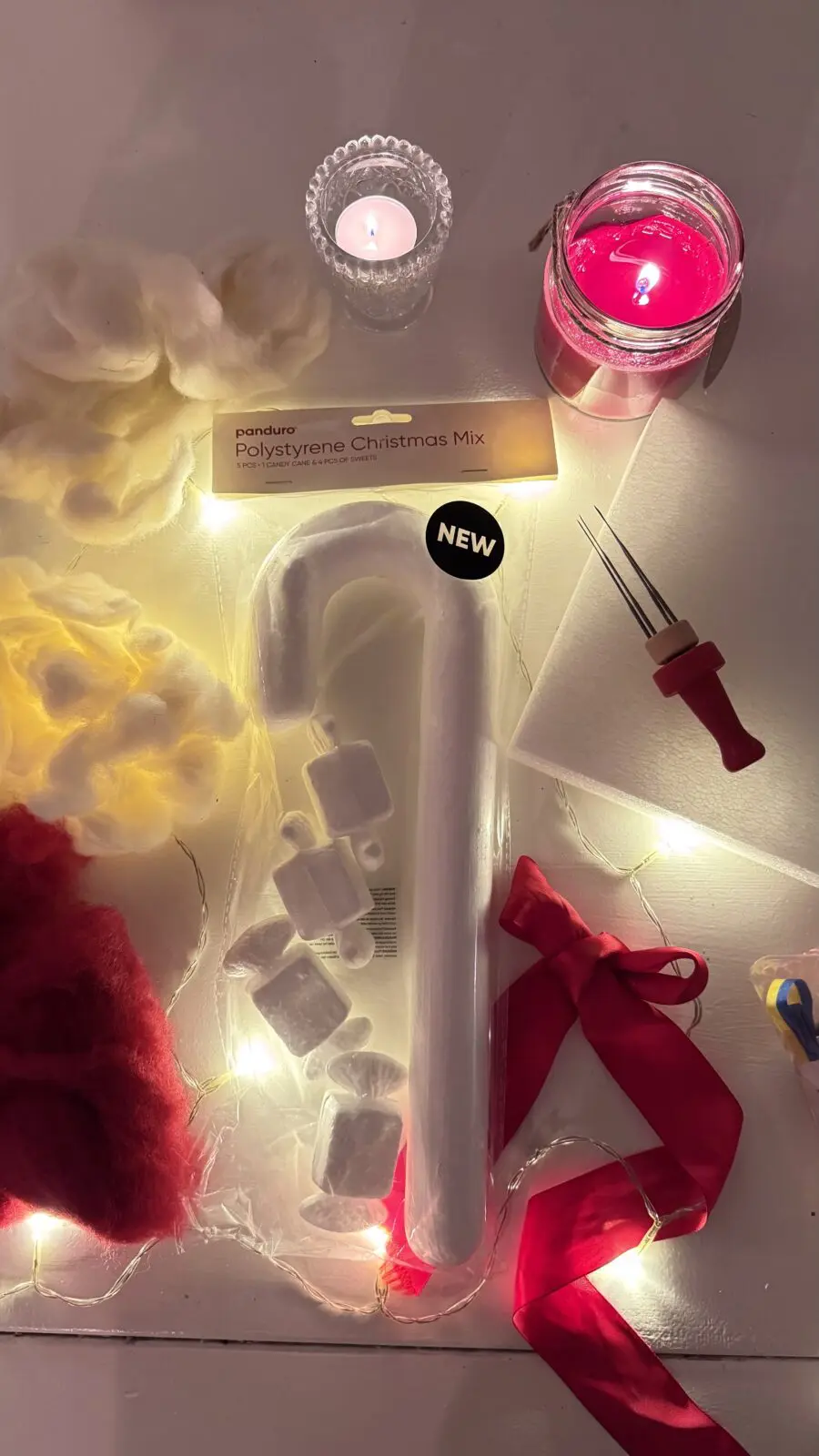 Material till julpyssel: styrolitpolkagris, ull i rött och vitt, filtnålar, ljusslinga och rött sidenband.