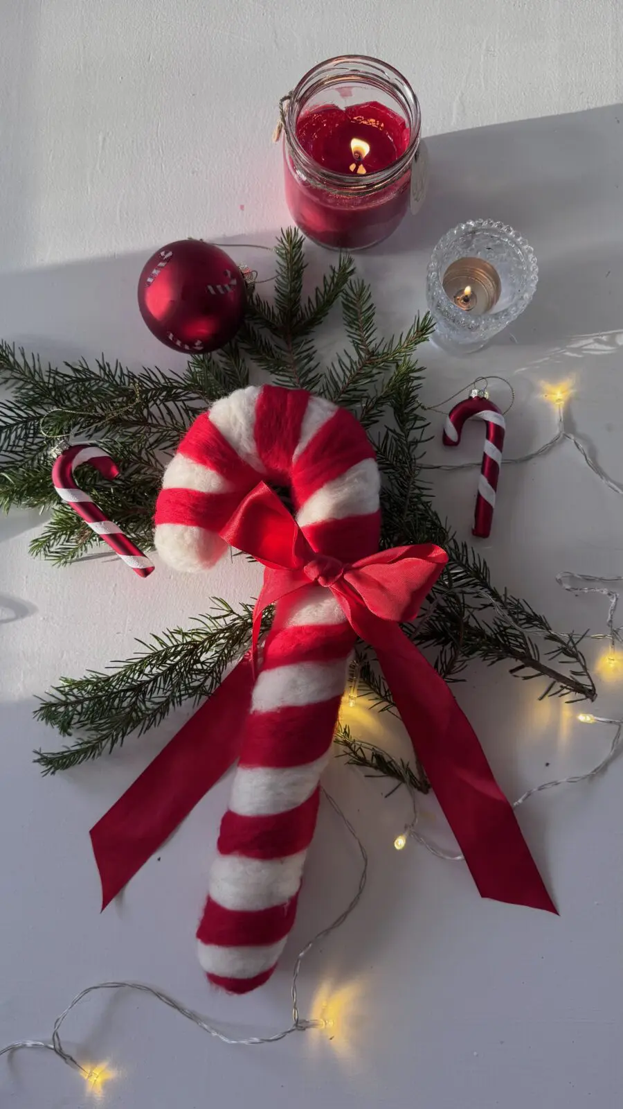 Färdig nålfiltad polkagris dekorerad med granris och röd sidenrosett som julkrans.