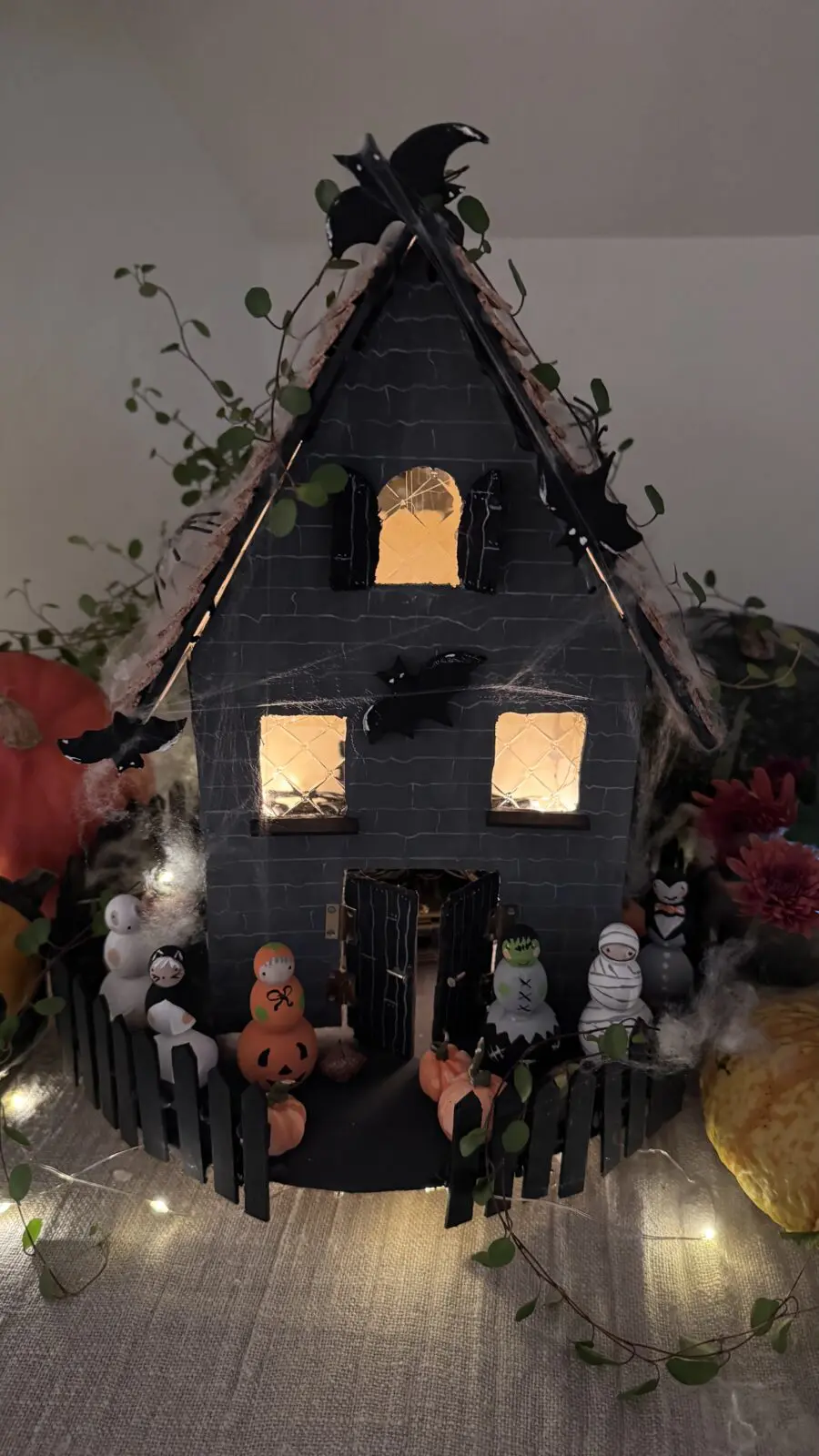 DIY spökhus i trä dekorerat med korktak, målade träfigurer, pumpor i lera och ljusslinga – enkelt Halloweenpyssel