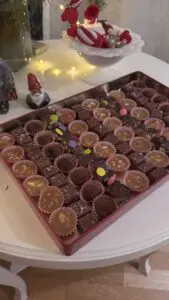 Traditionell plåtburk fylld med svenskt hemgjort julgodis: knäck, kola, tryfflar och rocky road bredvid en julillustration.