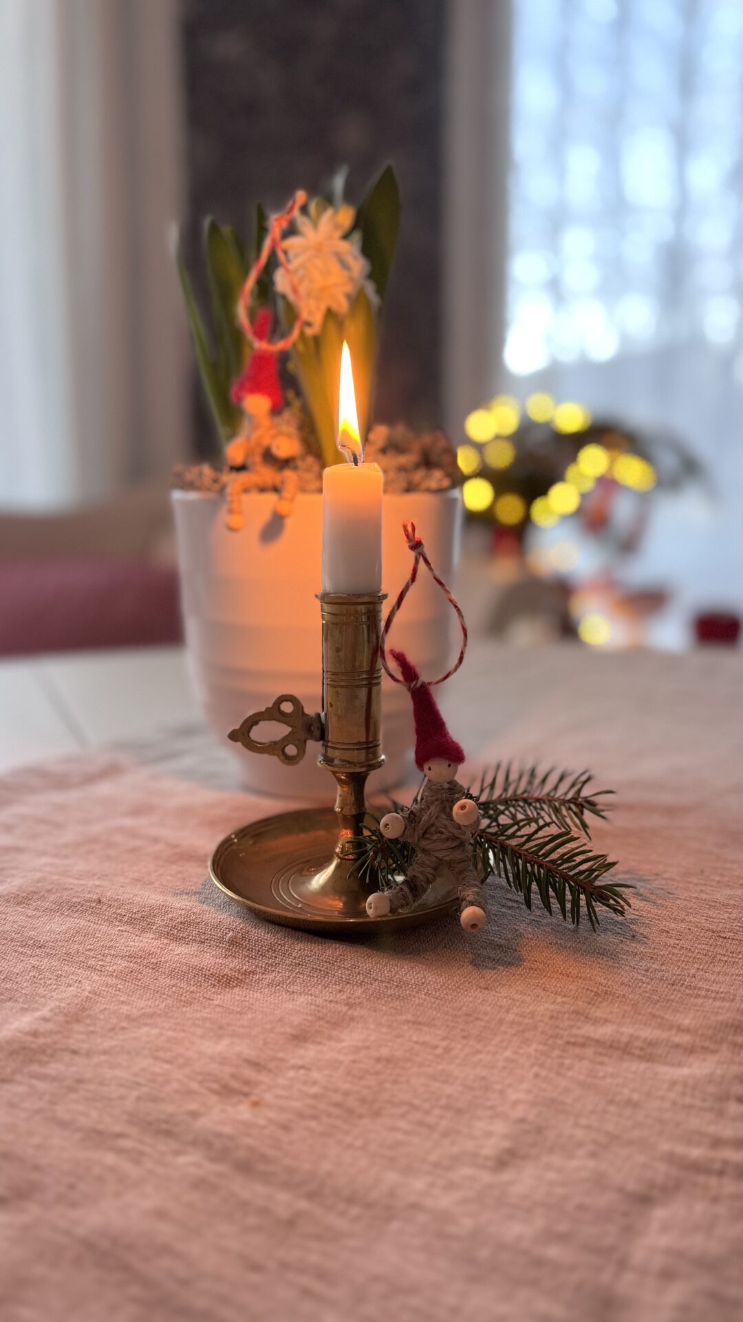 Minitomte av garn, piprensare och träkulor som dekoration bredvid hyacint och mässingsljusstake.